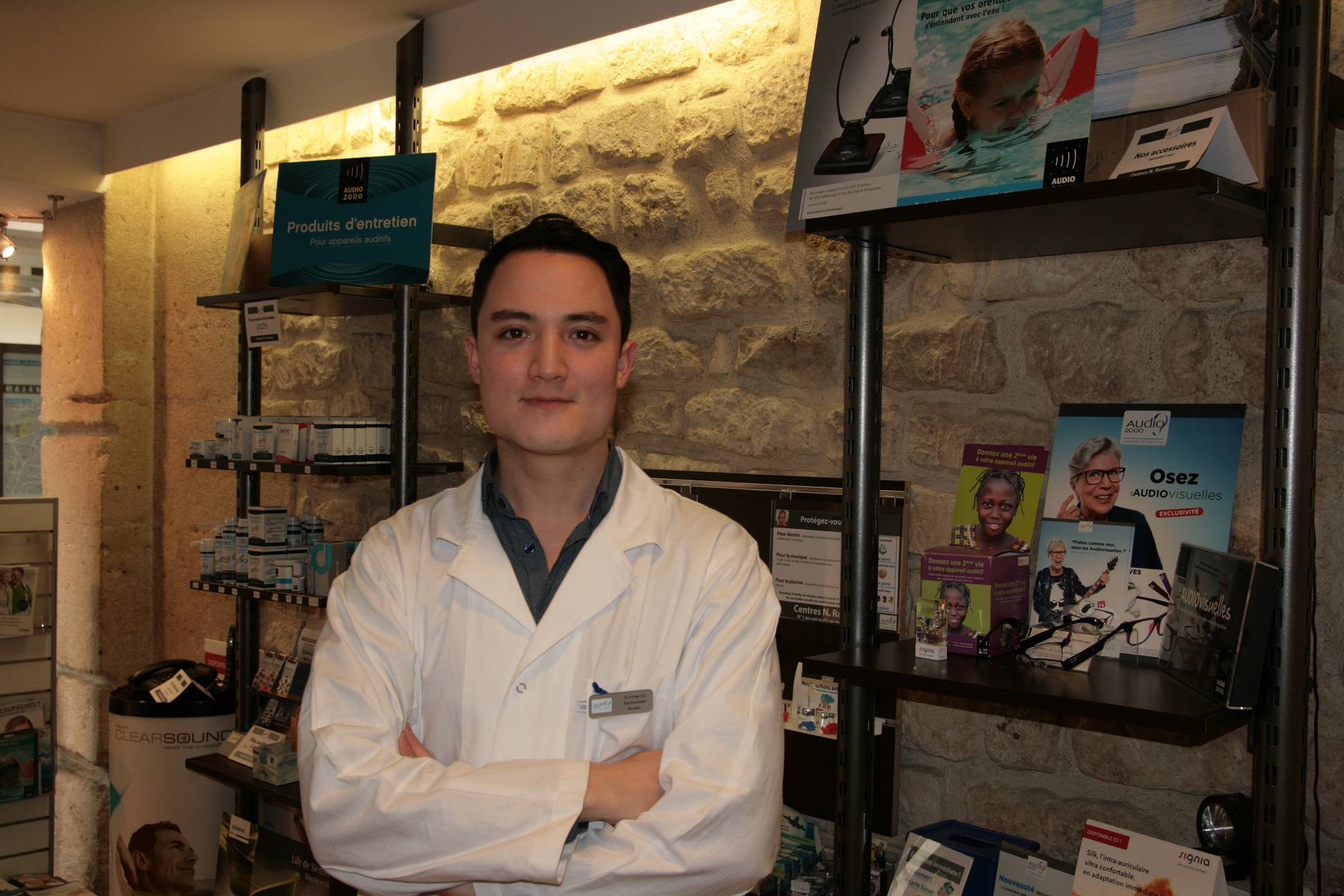 Aimeric, technicien audio, en blouse blanche devant le présentoir de produits d’entretien du centre